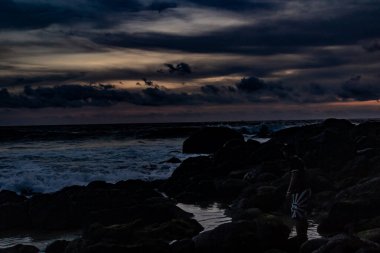 Phuket Tayland 'daki Karon Sahili' nin kuzeyinden karanlık bir gün batımı. Güneş, gökyüzünde kara bulutlarla dolu bir ışık çizgisi oluşturur. Işığın yansımaları sularda ve kumsalın ıslak kumlarında görülebilir..