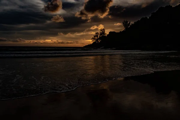 Karon Beach Phuket Tayland 'ın kuzey noktasında görkemli bir altın gün batımı. Dağlar ve ağaçlar siluet olarak görünür ve ışığın ve gölgenin yansımaları okyanusta ve ıslak kumlarda görülebilir..