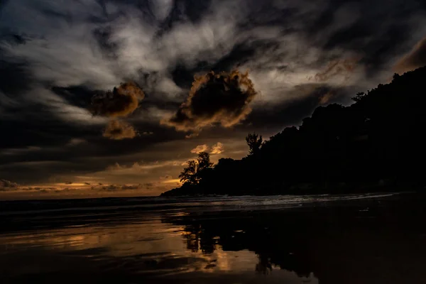 Karon Beach Phuket Tayland 'ın kuzey noktasında görkemli bir altın gün batımı. Dağlar ve ağaçlar siluet olarak görünür ve ışığın ve gölgenin yansımaları okyanusta ve ıslak kumlarda görülebilir..