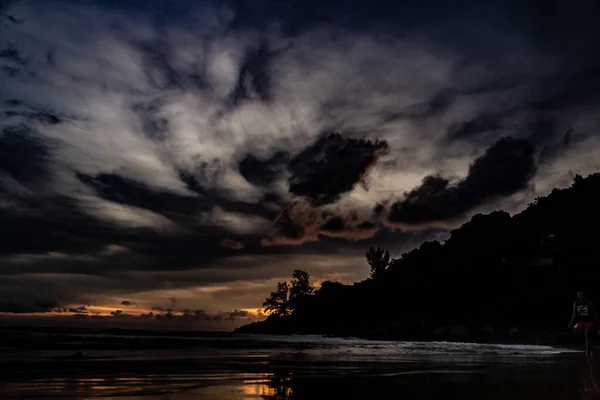 Karon Beach Phuket Tayland 'ın kuzey noktasında görkemli bir altın gün batımı. Dağlar ve ağaçlar siluet olarak görünür ve ışığın ve gölgenin yansımaları okyanusta ve ıslak kumlarda görülebilir..