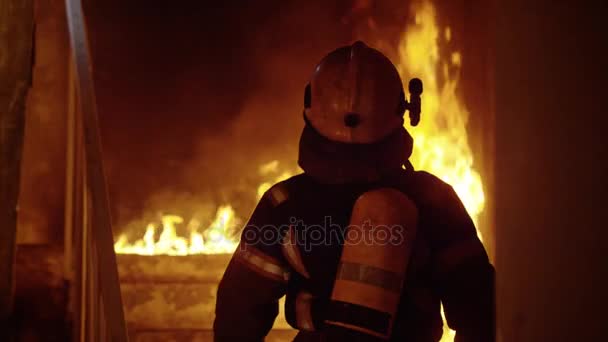 Bravo bombero asciende por las escaleras ardientes. Mirando alrededor inspeccionando el edificio. Llamas abiertas en segundo plano . — Vídeo de stock