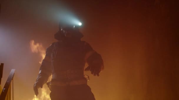 Bravo bombero con linterna encendida en su casco corre por las escaleras ardientes. El fuego está furioso. En cámara lenta . — Vídeo de stock