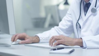 Beyaz saçlı kıdemli doktor ve masaüstü bilgisayarlarda çalışma Yardımcısı close-up. Açık renklerle çalışma Office yaktı.