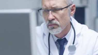 Kişisel bilgisayarınızda çalışan beyaz saçlı Doktor yakın çekim portre. Ofisinin parlak olduğunu ve ışık.