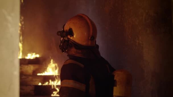 Porträt eines tapferen Feuerwehrmannes, der ein brennendes Gebäude inspiziert. Die Taschenlampe wird eingeschaltet und er blickt in die Kamera. Zeitlupe. — Stockvideo