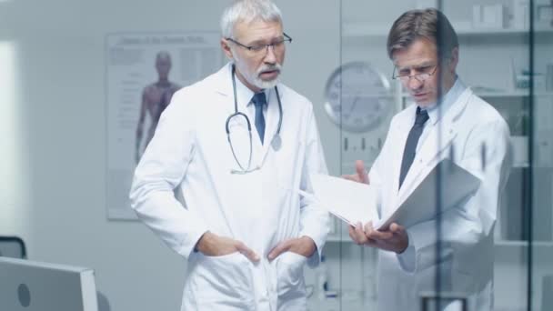 Two Specialist Doctors Discussing Patient's Log. Both are Senior and Experienced. Their Office Looks Modern and Respectable. — Stock Video