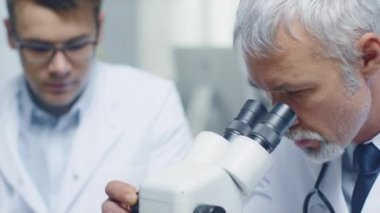 Kıdemli erkek doktor sağlık sorunu araştırma mikroskobu yürütmektedir. Genç asistanı ilgili verileri denetler.