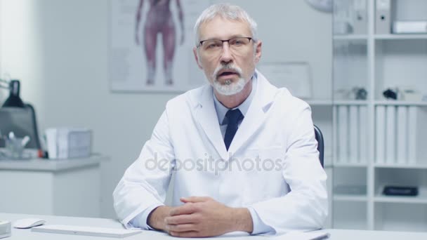 Experimentado Gray Haired Senior Medical Practitioner Talking Into Camera. Tiro de retrato en oficina moderna y ligera . — Vídeos de Stock