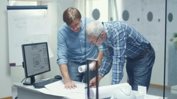 Dos ingenieros superiores trabajan con esquemas y planes de pie sobre la mesa de trabajo. Ellas tienen discusiones sobre el tema de varios asuntos técnicos relacionados con su proyecto . — Vídeo de stock