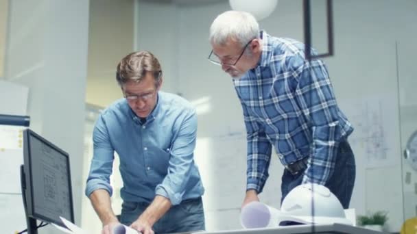 Due ingegneri senior lavorano con schemi e schemi mentre sono in piedi sopra il tavolo di lavoro. Hanno una discussione sul tema di varie questioni tecniche riguardanti il loro progetto. Girato al rallentatore . — Video Stock