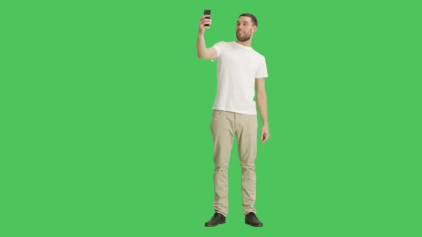 Largo tiro de un hombre elegante guapo tomando selfies en un fondo de pantalla verde . — Vídeos de Stock