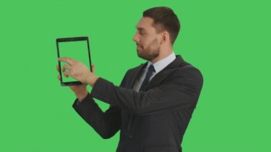 Tablet bilgisayar tek elle tutarak ve hareketleri ile başka bir dokunmadan Swiping yapma yakışıklı bir işadamı orta vurdu. Tablet ve arka plan yeşil ekran vardır.