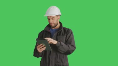 Bir yakışıklı işçi giyen beyaz zor şapka kullanarak Tablet bilgisayar yapma Swiping hareketleri üzerine orta vurdu. Yeşil ekran arka plan üzerinde ateş.