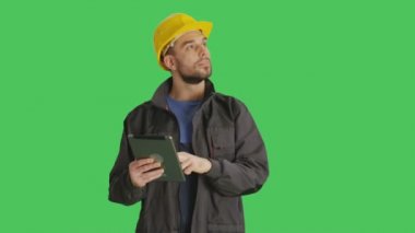 Bir yakışıklı işçi giyen sarı zor şapka kullanarak Tablet bilgisayar yapma Swiping hareketleri üzerine orta vurdu. Yeşil ekran arka plan üzerinde ateş.