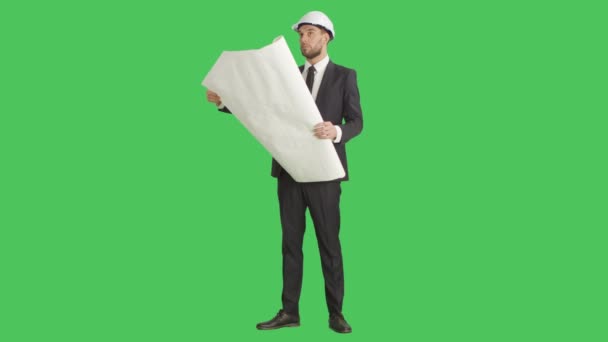 Colpo lungo di un uomo d'affari serio in un cappello duro Confronto circostante con cianografie che sta tenendo. Lo sfondo è schermo verde . — Video Stock