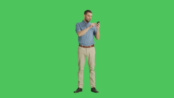 Long Shot of a Handsome Man Holding Smartphone with One Hand and Making Swiping Touching Gestures with Another. Tableta y fondo son pantalla verde . — Vídeo de stock