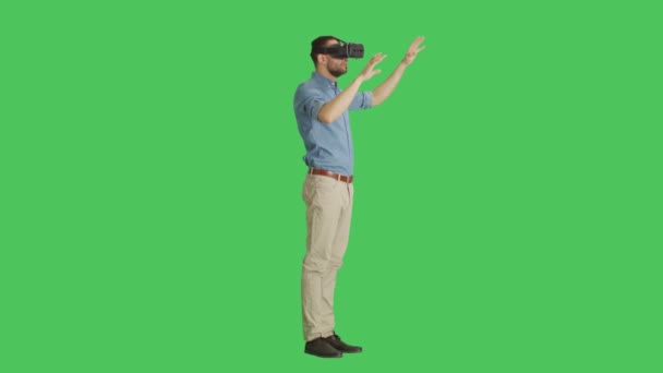 Die lange Aufnahme eines gutaussehenden Mannes mit Virtual-Reality-Brille interagiert mit der Außenwelt, während die Kamera um ihn herum rotiert. Hintergrund ist Green Screen. — Stockvideo