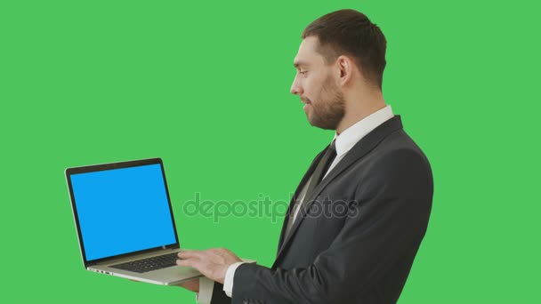 Medium Shot of a Handsome Businessman Holding Laptop Working with a Touchpad. We See Notebook's Blue Screen, All Shot on a Green Screen Background. — Stock Video