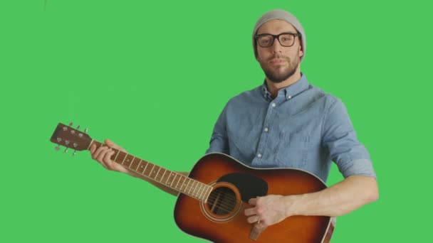 中期拍摄的一个年轻的天才音乐家，戴着帽子和眼镜弹吉他。背景是绿色屏幕. — 图库视频影像