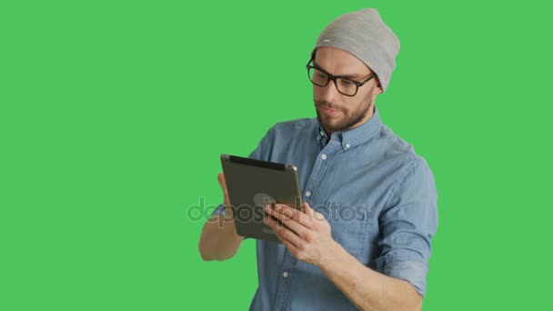 身に着けている帽子とメガネのタブレット コンピューターを使用してスタイリッシュな男のミディアム ショット。背景がグリーン スクリーンです。. — ストック動画
