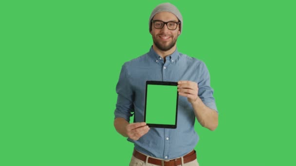 Mittendrin ein lächelnder junger Mann mit Brille, der Tablet-Computer mit grünem Bildschirm präsentiert. Green Screen im Hintergrund. — Stockvideo