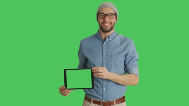 Mittendrin ein lächelnder junger Mann mit Brille, der Tablet-Computer mit grünem Bildschirm präsentiert. Green Screen im Hintergrund. — Stockvideo