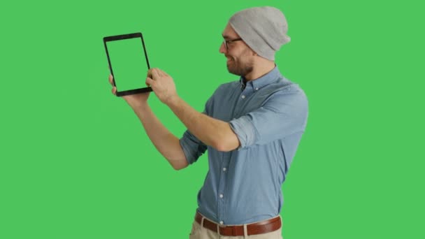 Die mittlere Einstellung zeigt einen stilvollen Mann mit Hut und Brille, der mit einer Hand einen Tablet-Computer hält und mit der anderen berührende Gesten macht. Tablet und Hintergrund sind grüne Bildschirme. — Stockvideo