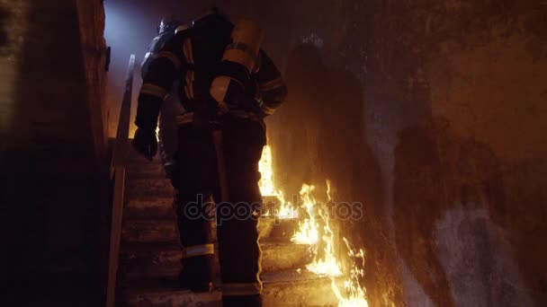 Dos bomberos fuertes subiendo las escaleras en el edificio en llamas. Las escaleras arden con llamas abiertas. En cámara lenta . — Vídeo de stock