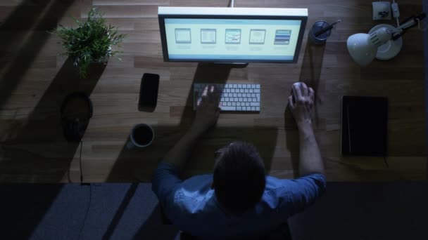 Bovenaanzicht van creatieve ontwerper werken op zijn bureaubladcomputer bij nacht. Zijn tafel wordt verlicht door koude blauw licht van buiten. — Stockvideo