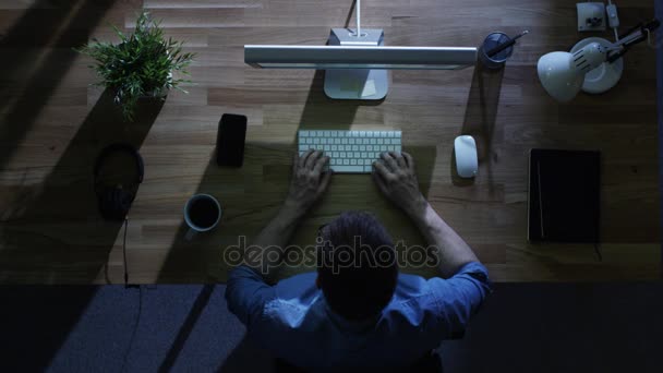 Draufsicht auf einen jungen Studenten, der nachts an seinem Desktop-Computer mit grünem Bildschirm arbeitet. sein Tisch wird von kaltem blauem Licht von außen beleuchtet. — Stockvideo