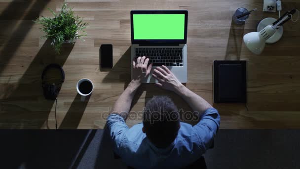 Vista dall'alto dello studente maschio che lavora al suo computer desktop con lo schermo verde finto di notte. La sua tavola è illuminata dalla luce blu fredda dall'esterno . — Video Stock