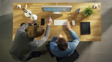 Üstten Görünüm iki grafik tasarımcıları iş üstünde okul sırası bilgisayar tartışıyor. Ayrıca tablo yalan Tarih: defter, Smartphone, kulaklık.