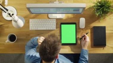 «Ana sayfa» yeşil Mock-up Tablet bilgisayarınızla bakarak genç yaratıcı tasarımcı görünümünü ekran oturma onun masasında. Dizüstü bilgisayar, kişisel bilgisayar ve kahve fincanı da masaya mevcut.