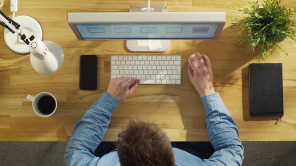 Bovenaanzicht van een softwareingenieur werkt op zijn bureaubladcomputer. Ook op de tafel ligt Smartphone en laptop. Tabel gemaakt van mooie hout. — Stockvideo