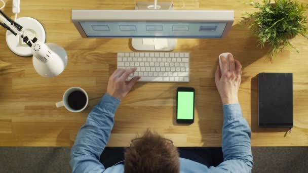 Vista dall'alto del Software Engineer Lavorando al suo computer desktop, beve caffè. Anche sul tavolo si trova Smartphone con finto schermo verde . — Video Stock