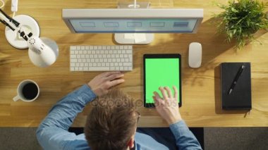 Ana sayfa görünümü genç yaratıcı tasarımcı dokunarak Mock-up yeşil olan bir Tablet bilgisayarda ekran oturma onun masasında. Dizüstü bilgisayar, kişisel bilgisayar ve kahve fincanı da masaya mevcut.