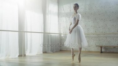 Genç ve güzel balerin dans ediyor enerjik ama incelikle Pointe bale ayakkabıları üzerinde o dönüyor. O beyaz Tutu elbise giyiyor. Sunny ve Modern stüdyom.