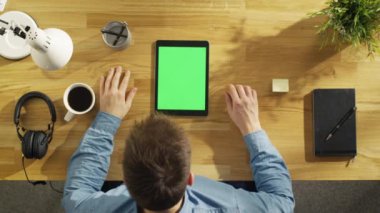 Üstten Görünüm yaratıcı gencin masasında oturan onun yeşil ekran Tablet bilgisayar üzerinde çalışıyor. O kalemi tutan ve kahve içiyor.