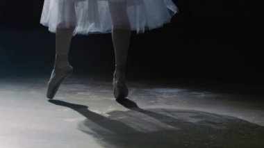Yakın çekim Shot balerin'ın bacakları. O dans ve Pointe bale ayakkabılarını spot üzerinde karanlık dön. O beyaz Tutu elbise giyiyor. '. Ağır çekimde.