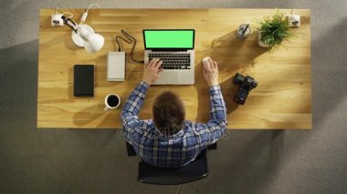 Onun Laptop ile yeşil ekranda üstten görünüm genç fotoğrafçı işleme fotoğrafları. Kamera, dış sabit disk ve defter onun yanında yalan.