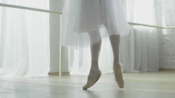 Primer plano de las piernas de la bailarina. Ella baila en sus zapatos de ballet de punta. Lleva un vestido blanco tutú. Grabado en un luminoso y soleado estudio moderno. En cámara lenta . — Vídeos de Stock