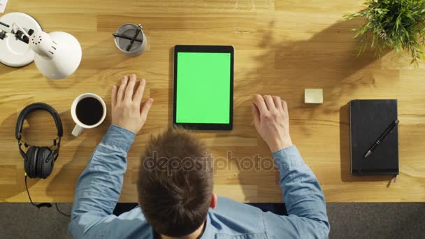 Вид зверху юнак творчої роботи над його зелений екран планшетного комп'ютера, сидячи на столі. Він тримає його пера і п'є каву. — стокове відео