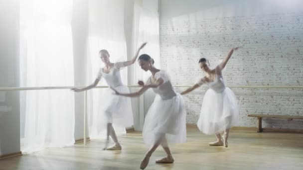 Drei junge und hinreißende Ballerinen, die synchron tanzen. Sie tragen weiße Tutu-Kleider. aufgenommen an einem sonnigen Morgen in einem hellen und geräumigen Studio. — Stockvideo