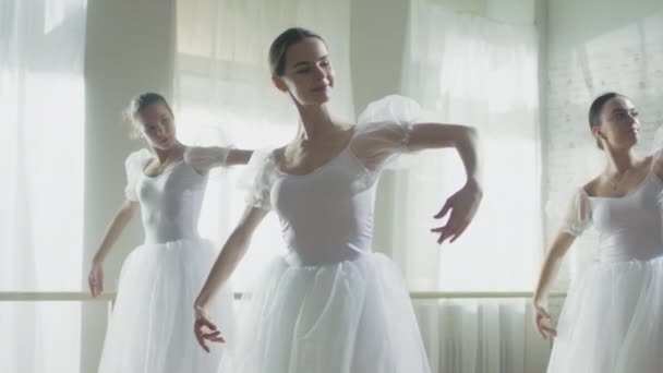 三个年轻和华丽芭蕾舞演员同步跳舞。他们穿着白色短裙礼服。在一个晴朗的早晨，在明亮和宽敞的工作室拍摄。在慢动作. — 图库视频影像