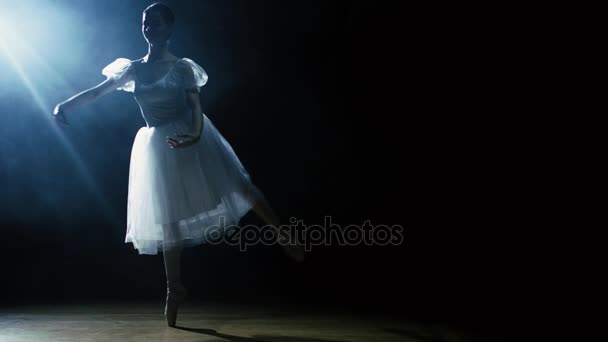 优雅地在聚光灯下，黑暗笼罩着她的美丽年轻的芭蕾舞演员共舞。她是穿着白色短裙裙子在灯光下闪闪发光。在慢动作. — 图库视频影像