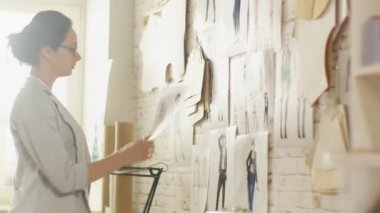 Her proje ve onları duvara sabitlenmesi için kadın moda tasarımcısı seçme skeçler. Sunny, dikiş makinesi duruyor masada onun stüdyom.