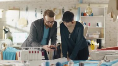 Kadın ve erkek moda danışmanlık Smartphone ve malzeme seçimi Tasarımcısı / kumaşlar için onların yeni giyim koleksiyonu. Sunny stüdyosudur. Renkli kumaş, giyim asılı ve dikiş öğeler görünür olur.