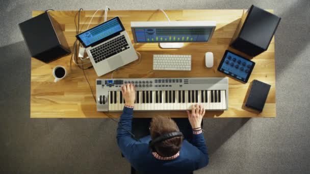 Вид сверху на человека, создающего музыку в своей студии, играющего на музыкальной клавиатуре. Его студия выглядит солнечно и приятно . — стоковое видео