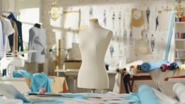 Zoom sur un mannequin sur mesure qui se tient dans un studio lumineux et ensoleillé. Différents articles à coudre et tissus colorés qui traînent, mannequins debout et croquis épinglés au mur . — Video