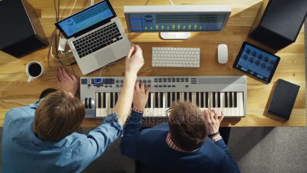 Вид зверху на двох звукорежисерів, що працюють у своїй сонячній студії. Вони грають на музичній клавіатурі і експериментують зі звуком . — стокове відео